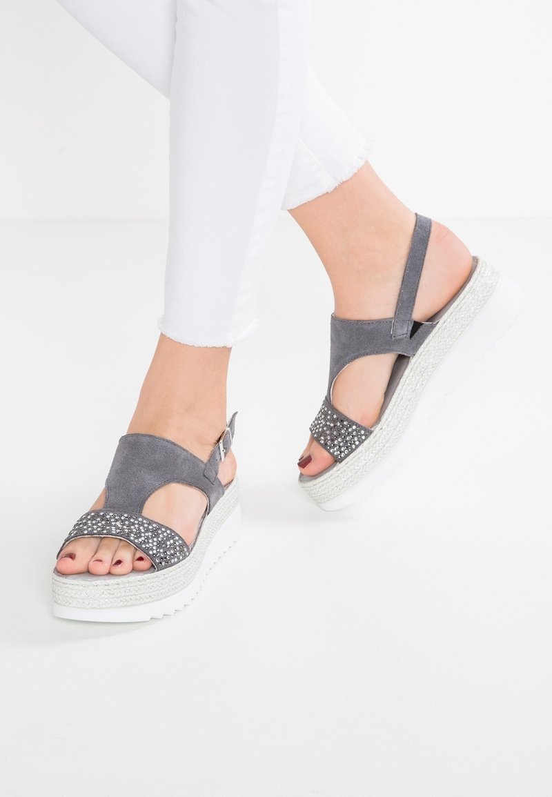 Sandales compensées en daim gris avec un design découpé et des accents de strass. Semelle plateforme blanche avec des détails texturés. Style ouvert à l'avant.