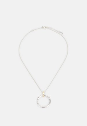 Tyndt sølvkædehalskæde med et stort sølvcirkelformet vedhæng, fastgjort med en lille gylden løkke, lagt fladt på en hvid baggrund.