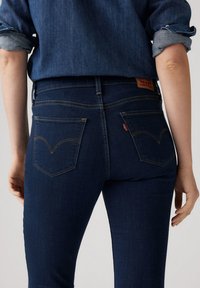 Tumman siniset farkut, joissa on korkea vyötärö, huomaamaton tikkaus ja kaksi takataskua, joissa on allekirjoitus kaareva muoto.