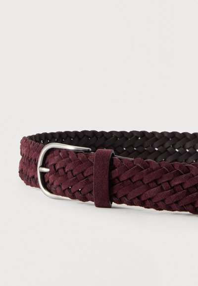 Ceinture en daim bordeaux foncé tressée avec boucle et passant en métal argenté sur un fond clair uni.