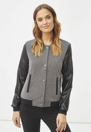 Chaqueta bomber de tela gris con mangas de cuero negro, dos bolsillos frontales y botones a presión, con puños y dobladillo acanalados.