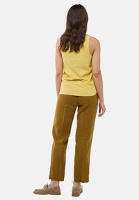 Un débardeur en coton jaune associé à un pantalon en lin brun-vert. L'ensemble présente une coupe décontractée et une texture lisse. Des chaussures décontractées complètent le look.