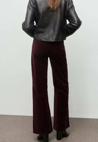 Pantalones acampanados de pana burdeos con bolsillos traseros, combinados con una chaqueta de cuero negra corta. Textura suave y ajuste de cintura alta.