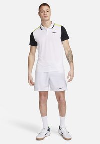 Polo shirt Nike da uomo bianco con maniche nere e dettagli giallo neon, abbinato a pantaloni corti bianchi. Tessuto morbido, colletto classico, logo sul petto.