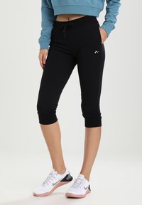 Leggings neri a vita alta con coulisse, orli a risvolto e un piccolo dettaglio con logo. Abbinati a scarpe da ginnastica bianche e grigie.