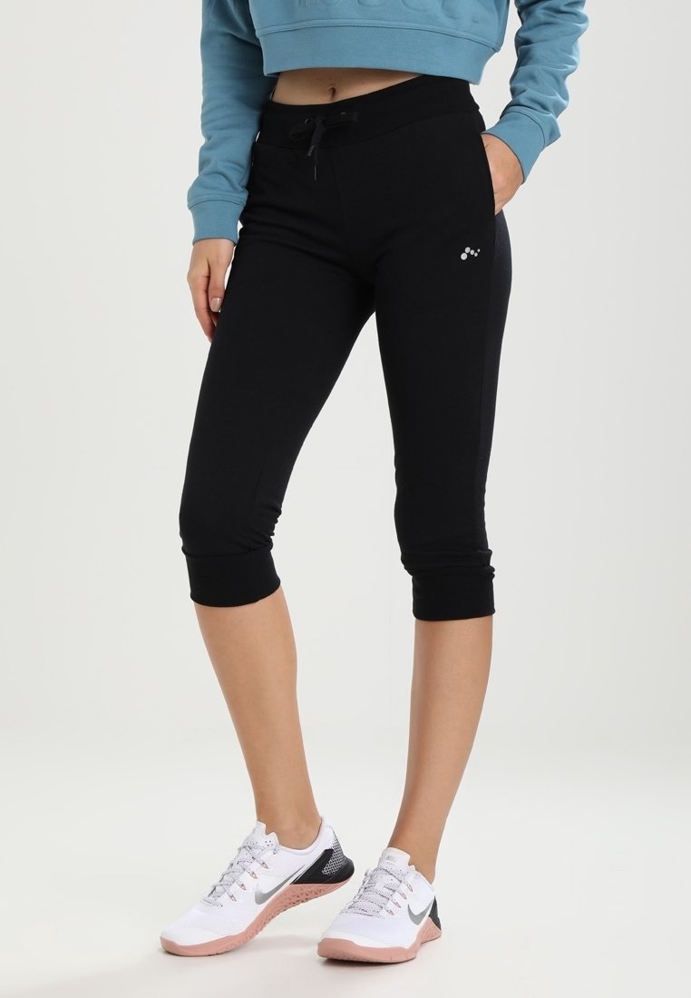 Leggings neri a vita alta con coulisse, orli a risvolto e un piccolo dettaglio con logo. Abbinati a scarpe da ginnastica bianche e grigie.
