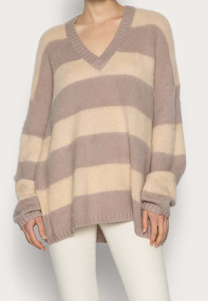 Överdimensionerad V-ringad tröja med breda horisontella beige och taupe-ränder, kombinerad med smalpassande off-white byxor.