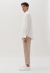 Witte lange mouwen shirt met knoopsokken, losse pasvorm, gecombineerd met lichtbeige broeken en witte sneakers. Eenvoudig ontwerp, geen patronen.