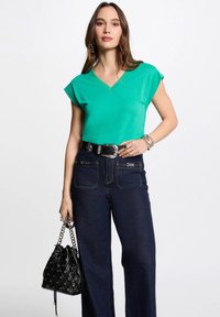 Groene v-hals top met korte mouwen, gecombineerd met hoge taille donkere denim wijde broek. Zwarte emmer tas met een kettinghandvat.