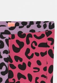 Leggings multicolor com tecido lilás e rosa, apresentando padrões ousados de manchas de leopardo pretas. Inclui um pequeno rótulo laranja na parte superior.