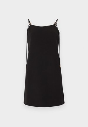 Svart ermeløs kjole med tynne dobbelt skulderstropper og dekorative bånd som henger ned på en ensfarget lys bakgrunn.