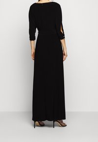 Vestido largo negro con mangas de tres cuartos, aberturas laterales y cintura ajustada. Tejido suave con un diseño fluido. Cierre con cremallera en la espalda.