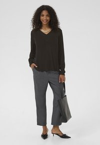 Zwarte blouse met lange mouwen en een V-hals, gecombineerd met grijze op maat gemaakte broek. Bevat een zilveren ketting en een zwarte handtas. Zwarte puntige flats.