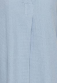 Tissu bleu clair avec un motif subtil en quadrillage et une couture verticale au centre, présentant un détail simple de bord d'encolure cousu.