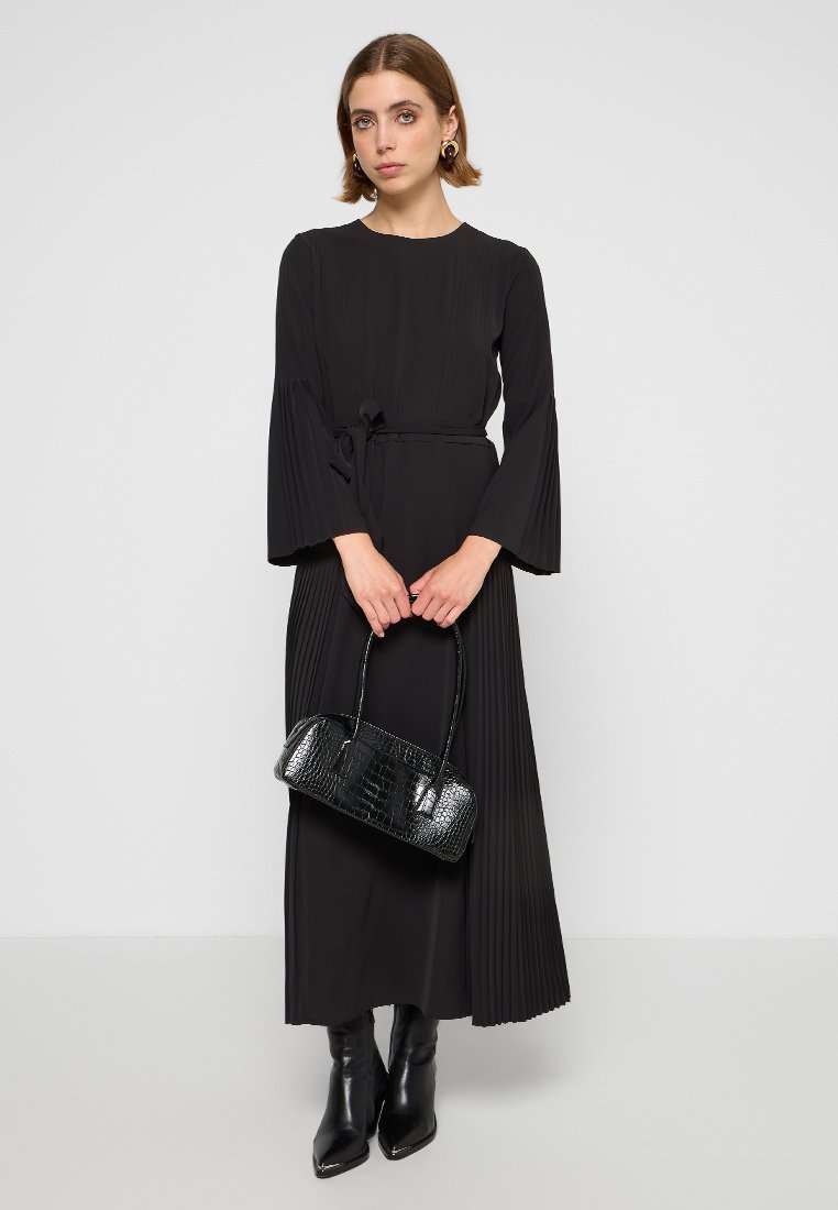 Abito nero a pieghe con maniche lunghe e cintura annodata in vita. Abbinato a una borsa nera con texture cocodrillo e stivali neri al ginocchio.