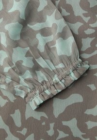 Manche avec poignet élastique sur tissu bleu clair présentant un motif camouflage abstrait gris avec un tissage texturé.