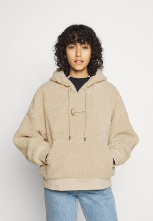 Beige fleece hettegenser med kengurulomme, snor i hetten og ribbestrikket kant. Har et gull-logo på brystet og mykt, teksturert materiale.