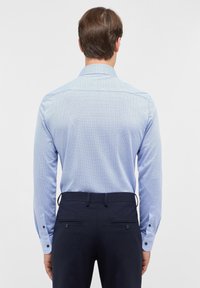 Camicia a maniche lunghe di un blu chiaro con motivo, abbinata a pantaloni blu scuro con due tasche posteriori.