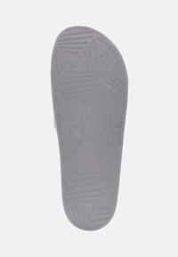 Semelle de chaussure grise avec des motifs triangulaires texturés et des rainures pour adhérence. Bord lisse menant à un orteil arrondi. Design à profil plat.