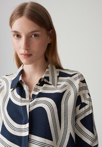 Camicia a maniche corte con bottoni, caratterizzata da una base crema con motivo geometrico blu navy, colletto a punta e realizzata in tessuto leggero.