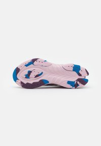 Semelle d'une chaussure de sport avec une base rose et des patchs en caoutchouc bleu et violet foncé sur fond blanc.