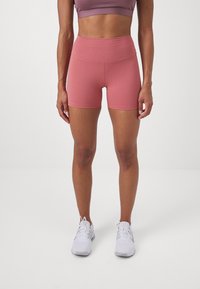 Shorts de talle alto ajustados en un suave tejido rosa. Textura lisa con costuras mínimas. Combinados con zapatillas deportivas blancas.