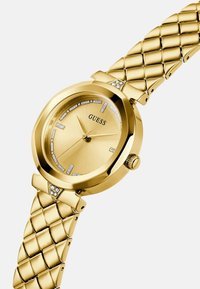 Kultakello, jossa on oktaalinen kuori ja kellotaulu, timanttisomisteiset tuntimerkit ja teksturoitu kultasävyinen ranneke.