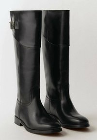 Knähöga svarta läderstövlar med en slät yta, en strukturerad form och en sidobuckle accent. Platt klack och rund tån design.