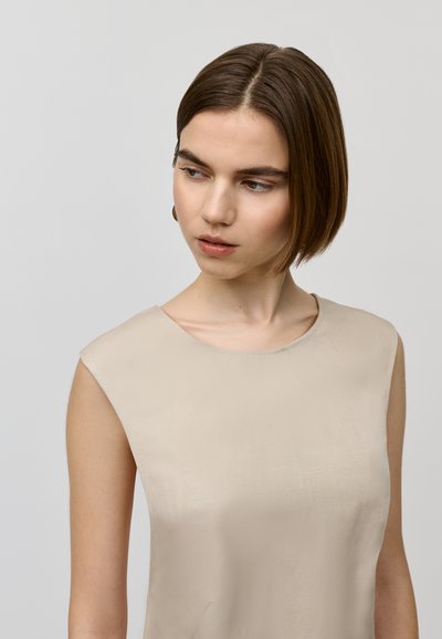 Beige mouwloos topje met een ronde halslijn, een soepele textuur en een subtiele glans. Eenvoudig ontwerp zonder zichtbare patronen of versieringen.