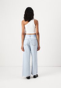 Vit ribbad one-shoulder crop top kombinerad med ljusblå vida jeans med fransar vid fållen och en standard femfickdesign.