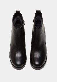 Botas de tobillo de cuero negro con una textura suave, punta redondeada y cremalleras laterales. Cuentan con un interior acolchado y un tacón bajo de goma.