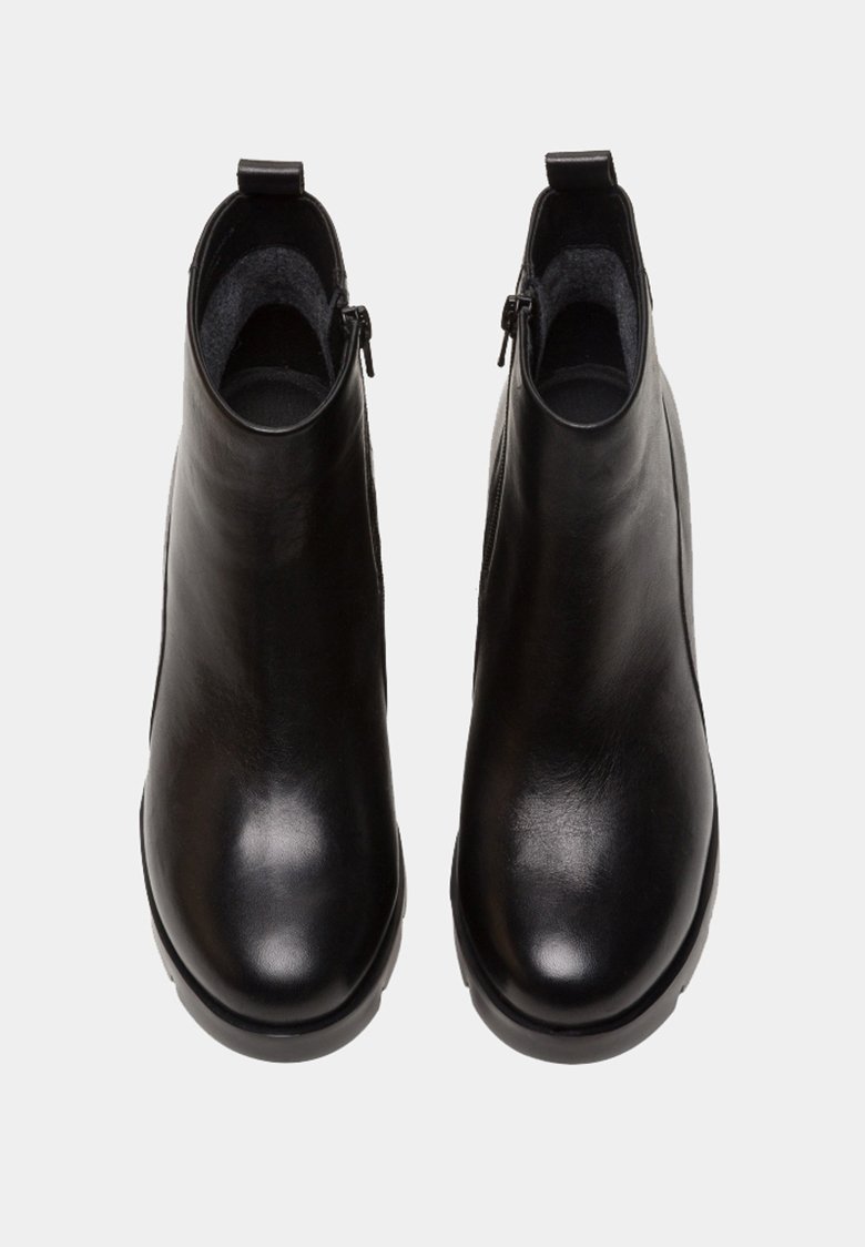 Botas de tobillo de cuero negro con una textura suave, punta redondeada y cremalleras laterales. Cuentan con un interior acolchado y un tacón bajo de goma.