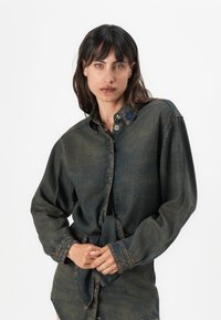 Cămașă din denim de culoare albastru închis, cu un nod în față, mâneci lungi, design cu nasturi și guler ajustat, având un patch cu logo pe partea stângă.