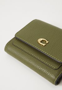 Green leather wallet with gold hardware, textured surface, and contrast stitching. Features a flap closure with a curved logo accent.