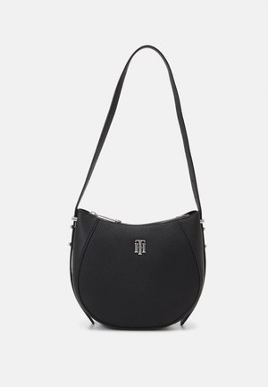 Sac porté épaule en cuir noir texturé avec une forme courbée, une fermeture éclair argentée et un petit logo monogramme à l'avant.