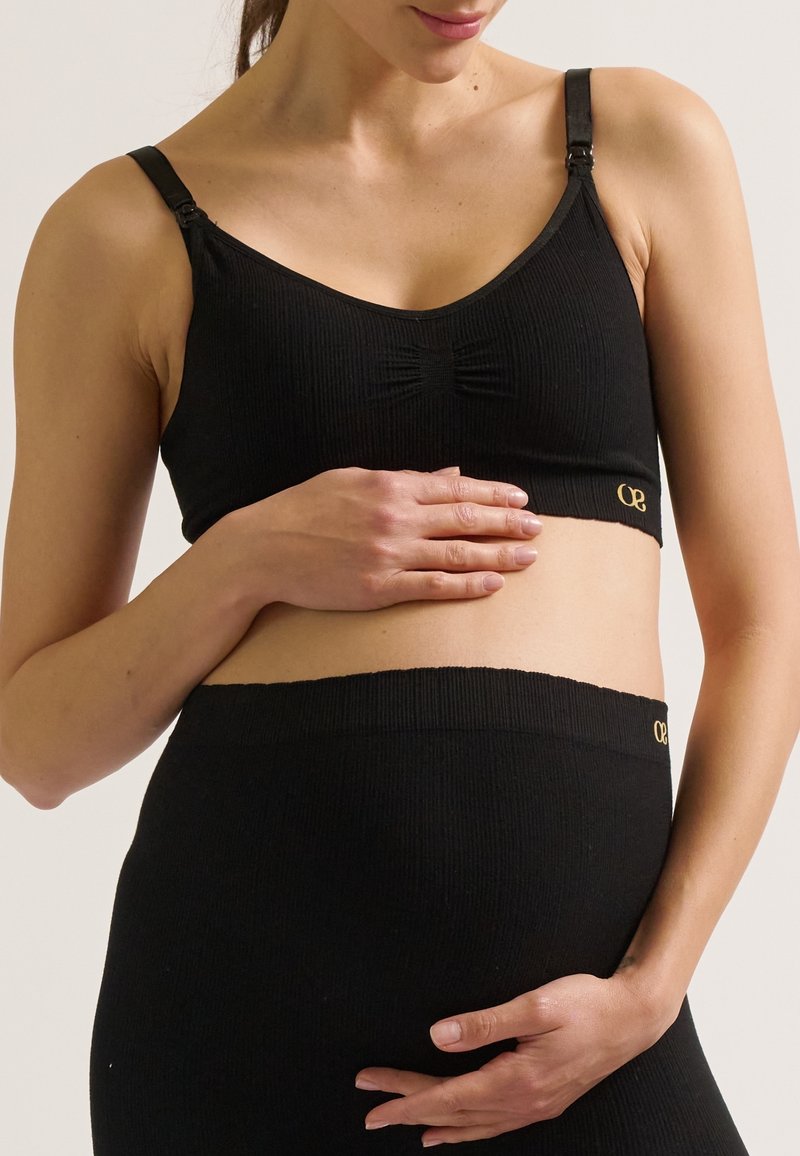 Soutien-gorge de maternité noir à côtes avec bretelles ajustables, détail nœud à l'avant et accent logo doré. Texture lisse, conçu pour le confort et le soutien.