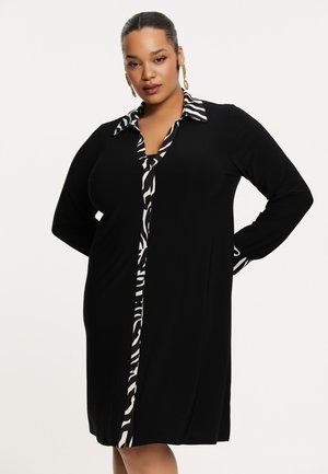 Robe noire à manches longues, avec un col imprimé zèbre et une patte de boutonnage. Fabriquée dans un matériau doux, présentant un design ajusté et une silhouette décontractée.