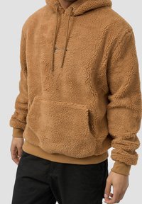 Ruskea fleece-huppari, jossa on teksturoitu pinta, säädettävät nauhat, etulokero ja ribatut hihansuut.