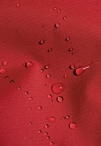 Wassertropfen, die auf einer glatten roten Stoffoberfläche perlen und dabei die Wasserbeständigkeit und die Textur des Stoffs hervorheben.