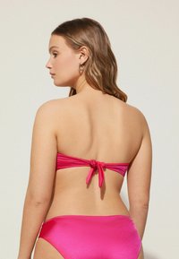 Conjunto de bikini en rosa brillante, que incluye un top bandeau con la espalda atada y una parte inferior a juego. Textura suave y brillante en toda la prenda.