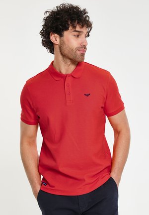 Camisa polo roja de algodón con cuello, tapeta de tres botones y detalle del logo en azul marino en el pecho. Mangas cortas, textura suave y diseño ajustado.