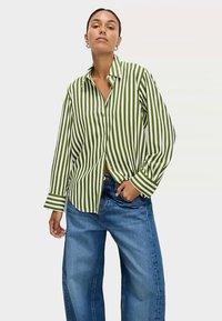 Zeleno-bíle pruhované tričko s dlouhým rukávem, volným střihem, zapínáním na knoflíky a klasickým límečkem. Kombinováno se širokými modrými džínami.