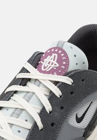 Grijze en lichtblauwe sneaker met een bovenwerk van suede en mesh, witte veters en een paarse label op de tong met een logo. Opvallende Swoosh-detail aan de zijkant.