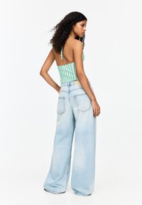 Groen en wit gestreepte haltertop met een aansluitende pasvorm, gecombineerd met lichtblauwe denim jeans met wijde pijpen en achterzakken.