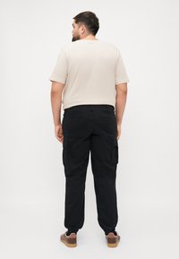 Zwarte cargo broek met zijzakken, elastische boorden, gecombineerd met een beige T-shirt met korte mouwen. Rond decolleté, comfortabele pasvorm.