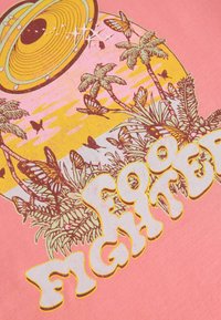 Rosa T-shirt med et grafisk design, der viser et UFO, palmetræer, sommerfugle og teksten "Foo Fighters" i fede, gule omridse bogstaver.
