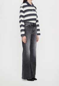 Polo a maniche lunghe a righe in blu navy e bianco, abbinato a jeans grigi a vita alta e a gamba larga. Tessuto in cotone liscio, vestibilità classica.