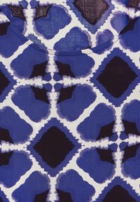 Blå och vit mönstrad tyg med abstrakta former; texturen verkar slät med en lätt lyster; rund halsringning synlig.