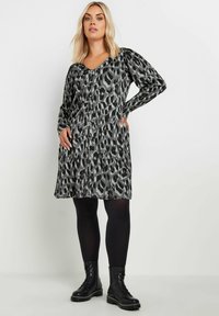 Sukienka w czarno-szare cętki z długimi rękawami, dekoltem w kształcie litery V i kieszeniami. Stylizowana z czarnymi, kryjącymi rajstopami i butami wojskowymi.