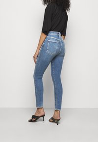 Jeans de mezclilla azul de cintura alta con un corte ajustado, con bolsillos traseros y un ligero desvanecimiento. Llevados con sandalias de tacón negras.